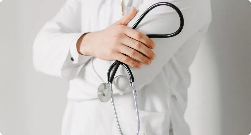 Médico sostiene un fonendoscopio sobre el pecho, listo para una consulta.